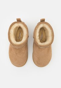 Botines de ante marrón con un suave forro de piel de color claro y una pequeña tira en la parte posterior. Forma redondeada y suelas planas.