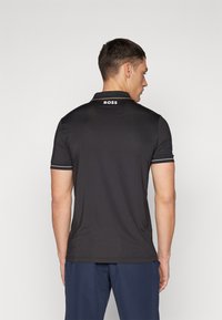 Polo negro con un diseño ajustado, mangas cortas, ribete del cuello en contraste y el logo "BOSS" en la parte posterior. Tela suave y ligera.