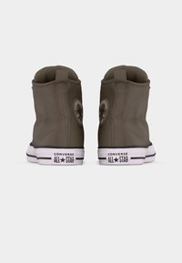 Smeđe Converse All Star tenisice s visokim gornjim dijelom prikazane sa stražnje strane, s bijelim potplatima i crnim logotipom na bijeloj pozadini.