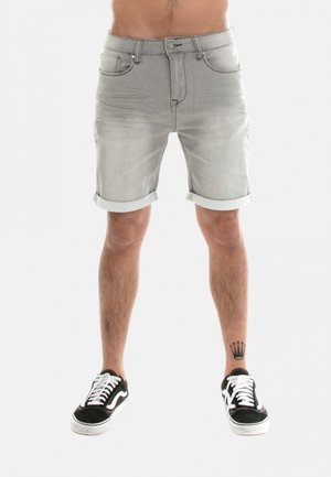 Shorts en denim gris clair avec des revers, poches avant et fermeture éclair. Portés avec des baskets noires à accents blancs.