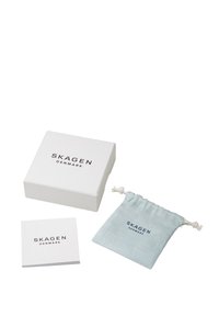 Bílá dárková krabice s nápisem "SKAGEN DENMARK" vytištěným nahoře, světle modrý sáček se stáhnutím na šňůrku a malý bílý leták.