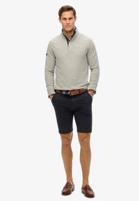 Lys grå langærmet polo med krave, marineblå shorts, brun læderbælte og loafers. Rene linjer og tætsiddende design hele vejen igennem.