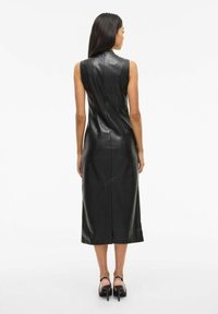 Zwarte leren mouwloze jurk met hoge kraag, aansluitende silhouet en knie-lengte zoom, met een centrale rugnaad detail.