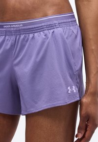 Κοντινή λήψη ενός ατόμου που φοράει αθλητικά σορτς Under Armour σε λεβάντα με ελαστική μέση και λογότυπο στο αριστερό πόδι.