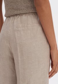 Pantalons en lin beige à coupe décontractée, dotés d'une taille élastique et d'une poche arrière unique. Le tissu a une finition texturée.