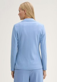 Light blue tailored blazer with a smooth texture, notch lapels, and long sleeves; features a central back seam and fitted silhouette.