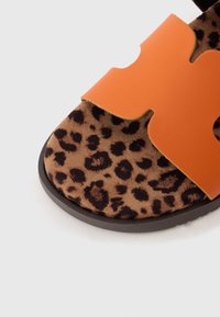 Sandal s leopard uzorkom sa smešnim ante insoleom i narančastim kožnim remenom s izrezbarenim dizajnom. Crna gumena potplata sa teksturiranim gripom.