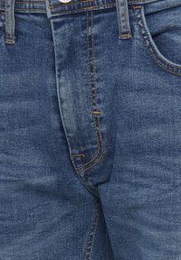 Vaqueros de mezclilla azul oscuro con diseño clásico de cinco bolsillos, costuras de cobre y cierre de botón en la cintura. Textura suave con un ligero desgaste.