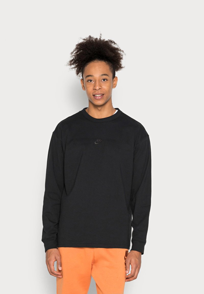 Schwarzes Nike-Shirt mit langen Ärmeln und Rundhalsausschnitt. Mit einem kleinen, geprägten Logo auf der Brust. Weicher Stoff mit lockerer Passform.