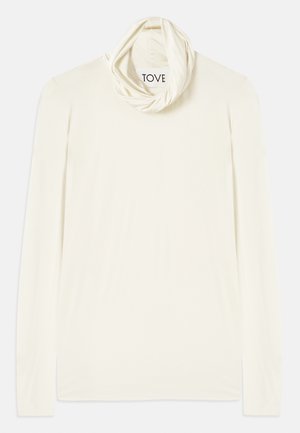 Dolga rokavica krema barve z drapirano, tubularno ovratnikom. Narejena iz mehkega blaga, ima gladko teksturo in oznako "TOVE."