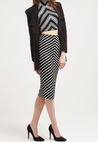 Ensemble de top court à rayures noires et blanches et de jupe crayon, associé à un blazer noir. Des talons complètent le look. Tissu lisse et design ajusté.