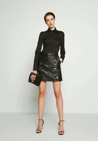 Czarna skórzana spódnica o fasonie ołówkowym, z zamkiem z przodu i dekoracyjnymi elementami. W połączeniu z dopasowanym czarnym topem z długim rękawem.