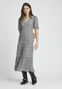 Robe maxi florale avec manches courtes, décolleté en V et taille froncée. Le tissu est léger avec un motif de fleurs noir et blanc.