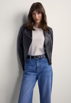 Czarna skórzana kurtka motocyklowa na białej koszulce, do tego jasnoniebieskie dżinsy z wysokim stanem i czarny pasek z okrągłą klamrą.