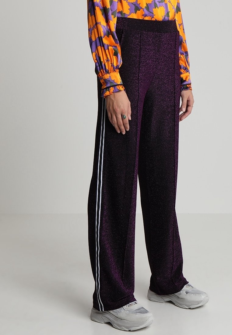 Lila glittriga byxor med en glänsande yta, som har vita sidostråk. Designen är vida ben och midjehöga, vilket ger en avslappnad passform.