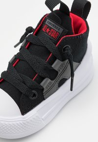 Czarne trampki z czerwonymi akcentami i szarymi detalami, z gumowym czubkiem, płaskimi czarnymi sznurówkami i fakturowaną białą podeszwą.