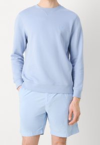Felpa azzurra in cotone, con colletto rotondo e polsini a costine. Abbinata a pantaloni corti azzurri coordinati.