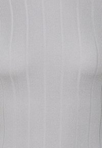 Haut en maille côtelée gris clair présentant des rayures verticales et une finition texturée, mettant en valeur une coupe ajustée et une surface lisse.