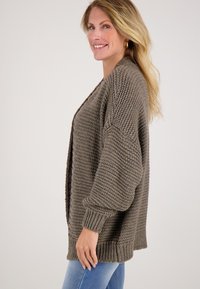 Bruine gebreide cardigan met een losse pasvorm, verlaagde schouders en ribbelmanchetten. Getextureerde stof met een chunky weefsel.