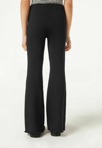 Pantalones de campana negros con textura acanalada y cinturilla elástica, que presentan una superficie texturizada y un acabado sin confeccionar en el dobladillo, vistos desde la parte posterior.