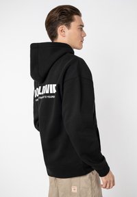 Black hooded sweatshirt with white text on the back. Features a relaxed fit and ribbed cuffs. Fabric appears soft and thick.