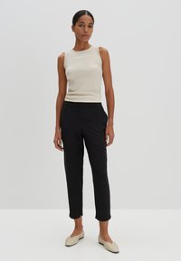 Débardeur côtelé beige clair associé à un pantalon noir ajusté et des ballerines crème. Design minimaliste avec des textures lisses et une silhouette ajustée.