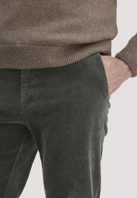 Donkergroene corduroy broek met subtiele verticale ribbels, gecombineerd met een lichtbruine trui. De outfit heeft zijzakken.