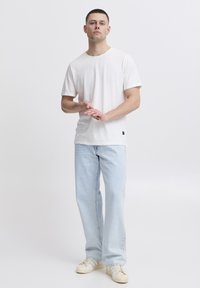 T-shirt bianca a girocollo con maniche corte, abbinata a jeans azzurri a gamba dritta. Indossata con sneakers beige con tre strisce.