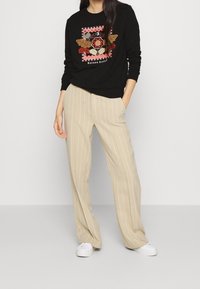 Sudadera negra con bordado floral y borde a cuadros, combinada con pantalones de pierna ancha a rayas beige y zapatillas blancas.