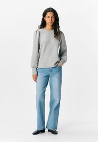 Grijze sweatshirt met uitlopende mouwen, gecombineerd met lichtblauwe flared jeans en zwarte schoenen, met een ontspannen pasvorm en een zachte textuur.