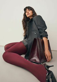 Bordeauxfarbene Strumpfhosen, schwarze Lackabsätze, dunkler Nadelstreifenblazer, Ledershorts, glänzende kastanienbraune Handtasche, glatte Texturen, minimalistischer Hintergrund.