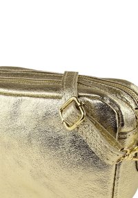 Gouden metallic handtas met een gladde, glanzende textuur, ritsluiting en een goudkleurige metalen bandaanhechting.