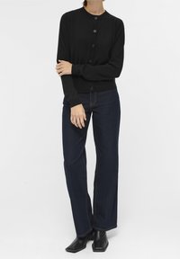 Schwarze gestrickte Strickjacke mit Rundhalsausschnitt und sieben Knöpfen, kombiniert mit dunkelblauen weit geschnittenen Jeans und schwarzen, eckigen Ankle Boots.