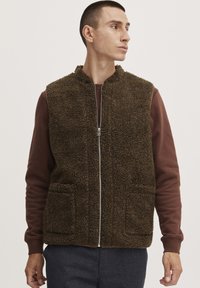 Brun fleece vest med høj krave, lynlås foran og to for-lommer. Bæret over en bordeaux langærmet top. Tekstureret og blød udseende.