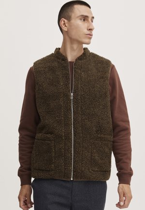Brown fleece vest with a high collar, front zipper, and two front pockets. Worn over a burgundy long-sleeve top. Textured, soft appearance.