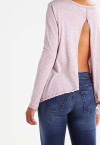 Ljusrosa långärmad topp med öppen ryggdesign. Mjuk, texturerad tyg. Matchad med mörkblå tajta jeans med bakfickor.