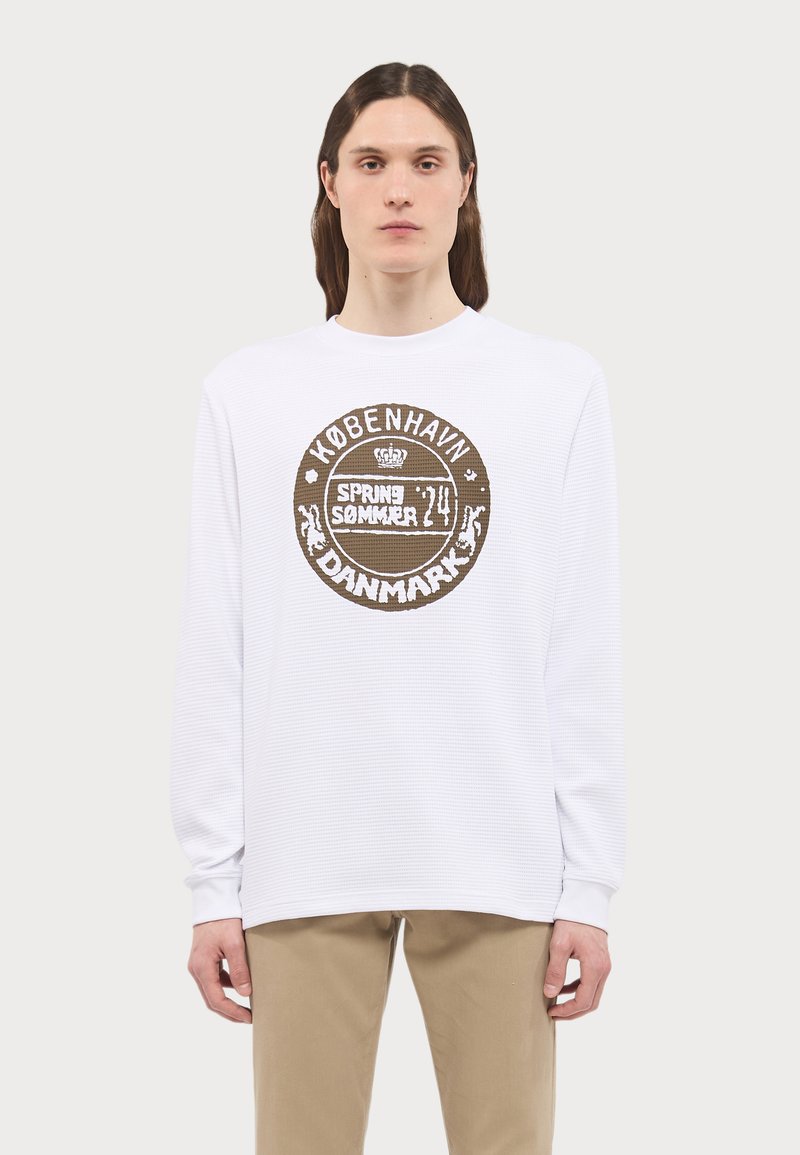 White long-sleeve shirt with textured fabric featuring a round graphic print in brown, stating "København SPRING SUMMER 24 DANMARK."