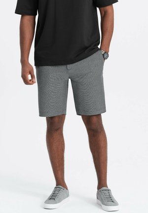 Shorts en pied-de-poule gris avec un devant plat, des poches latérales et une coupe régulière, associés à une chemise noire à manches courtes et des baskets grises.