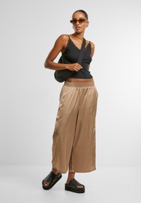 Black tank top with lace trim, beige satin wide-leg pants, black platform sandals, and tinted sunglasses. Model carrying a black shoulder bag.