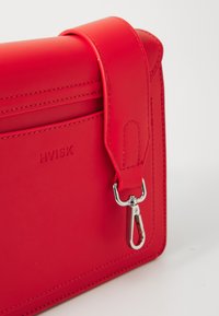 Röd läder crossbody-väska med en slät design, en stickad handtag och silverfärgad hårdvara. Har logotyp-embossing och en detalj med dragkedja.