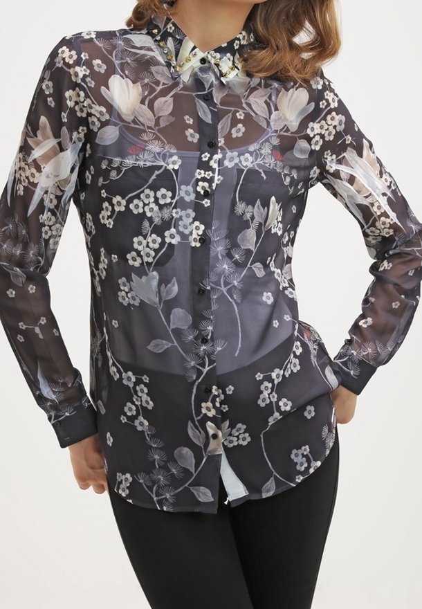 Durchsichtige schwarze Bluse mit floralen Mustern in Weiß und hellen Farben; verfügt über eine Knopfleiste, lange Ärmel und Besätze mit Nieten am Kragen.