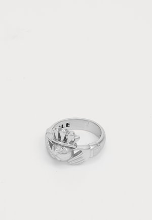 Bague Claddagh en argent représentant des mains tenant un cœur couronné sur un fond blanc uni.