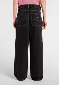 Black denim wide-leg pants with a high waist, featuring two back pockets and subtle contrast stitching. Soft texture and relaxed fit.