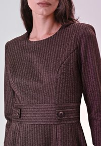 Bruine jurk met een visgraatpatroon, een ronde hals, lange mouwen en een tailleriem met twee knoopdetails.