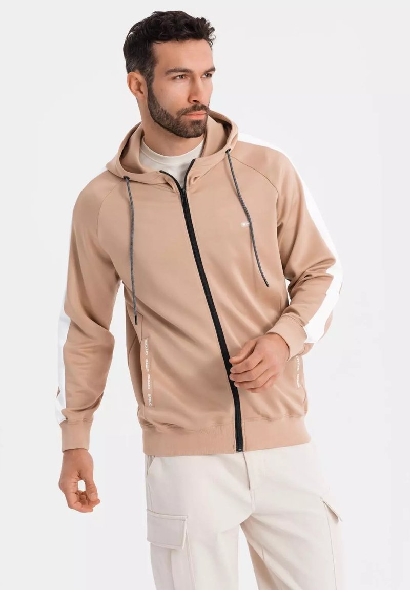 Felpa beige con zip e cappuccio regolabile, zip nera e strisce laterali bianche. Tessuto leggero, con dettagli del logo sulle maniche.