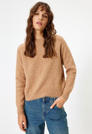 Brauner, weicher Pullover mit langen Ärmeln und Rundhalsausschnitt, kombiniert mit lässigen blauen Jeans im Relaxed Fit. Leichte Textur sichtbar.