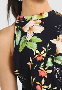 Blommönstrad tyg i marinblått, med stora beige och rosa blommor och gröna blad. Slät textur med ärmlös design.