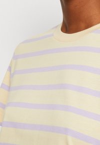 Short-sleeve shirt in light yellow with horizontal lavender stripes. Soft fabric and crew neck design with smooth texture.