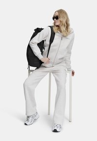 Harmaa huppari ja verkkarit, joissa on etuvetoketju, yhdistettynä mustaan reppuun ja valkoisiin lenkkitossuihin. Sujuva pinta, rento muotoilu.