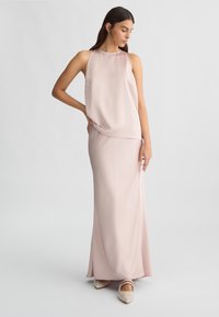 Abito senza maniche di un rosa pallido realizzato in tessuto morbido, caratterizzato da una silhouette fluida. Abbinato a scarpe a punta decorate.